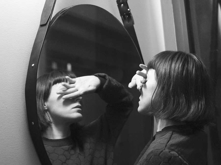woman in front of a mirror hiding her eyes with her arm, in black and white